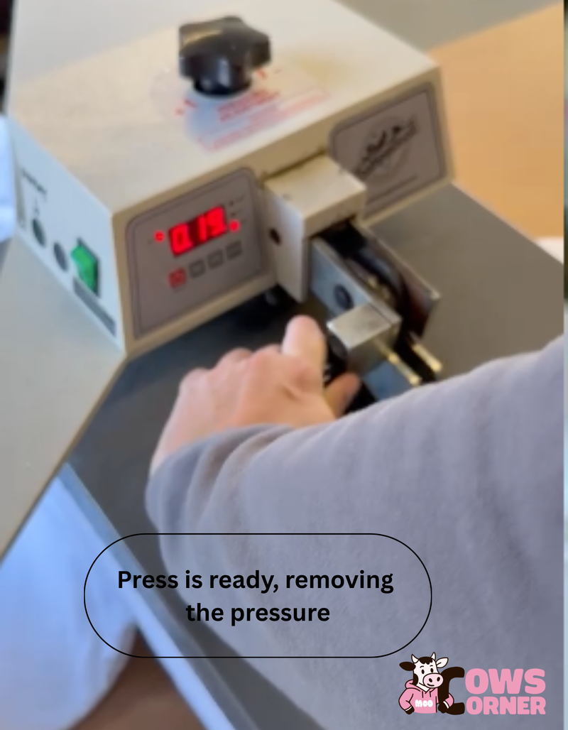 Person operating a heat press machine with digital display, text 'Press is ready, removing the pressure', and 'Cows Corner' logo.