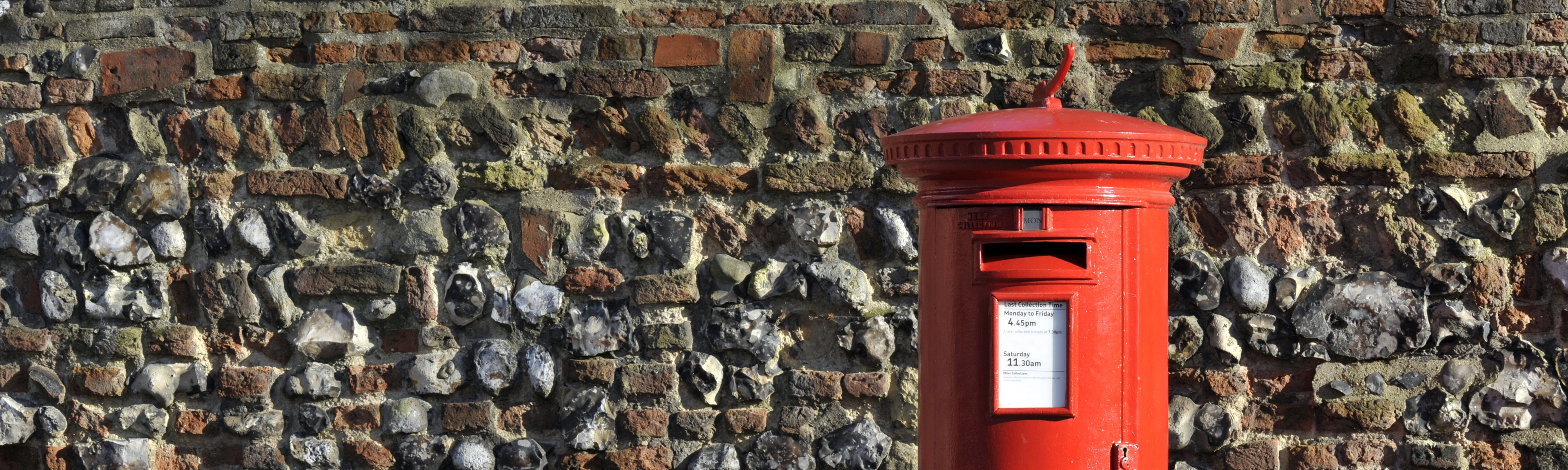 Red postbox against a stone wall enabling people to track their order with Cows Corner