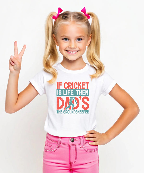 A little girl wearing a white t-shirt with If Cricket Is Life, Then Dad's The Groundskeeper on the front. A Funny Cricket T-Shirt, Premium Fabric, Multiple Junior Sizes