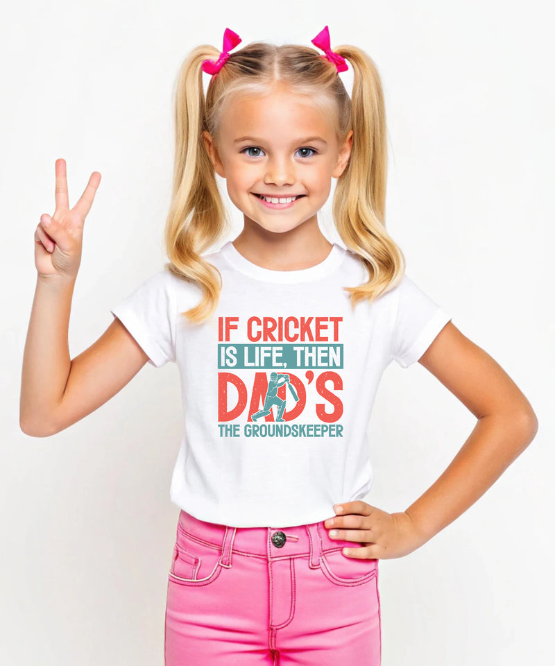 A little girl wearing a white t-shirt with If Cricket Is Life, Then Dad's The Groundskeeper on the front. A Funny Cricket T-Shirt, Premium Fabric, Multiple Junior Sizes