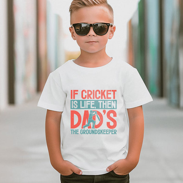 A little boy wearing a white t-shirt with If Cricket Is Life, Then Dad's The Groundskeeper on the front. A Funny Cricket T-Shirt, Premium Fabric, Multiple Junior Sizes
