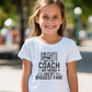 A little girl wearing a white t-shirt with the funny football slogan on the front saying 'Messi, Ronaldo…Nah ’My Dads the Real Goat!