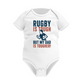 White baby onesie with rugby-themed text on a white background with a Cows Corner slogan saying Rugby is tough, but my dad is tougher