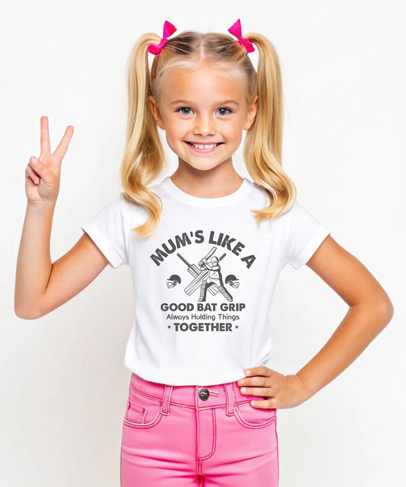 A little girl wearing a white t-shirt with Mums Like A Good Bat Grip, Always Holding Things Together on the front. A Funny Cricket T-Shirt, Premium Fabric, Multiple Junior Sizes, Perfect for Boys and Girls