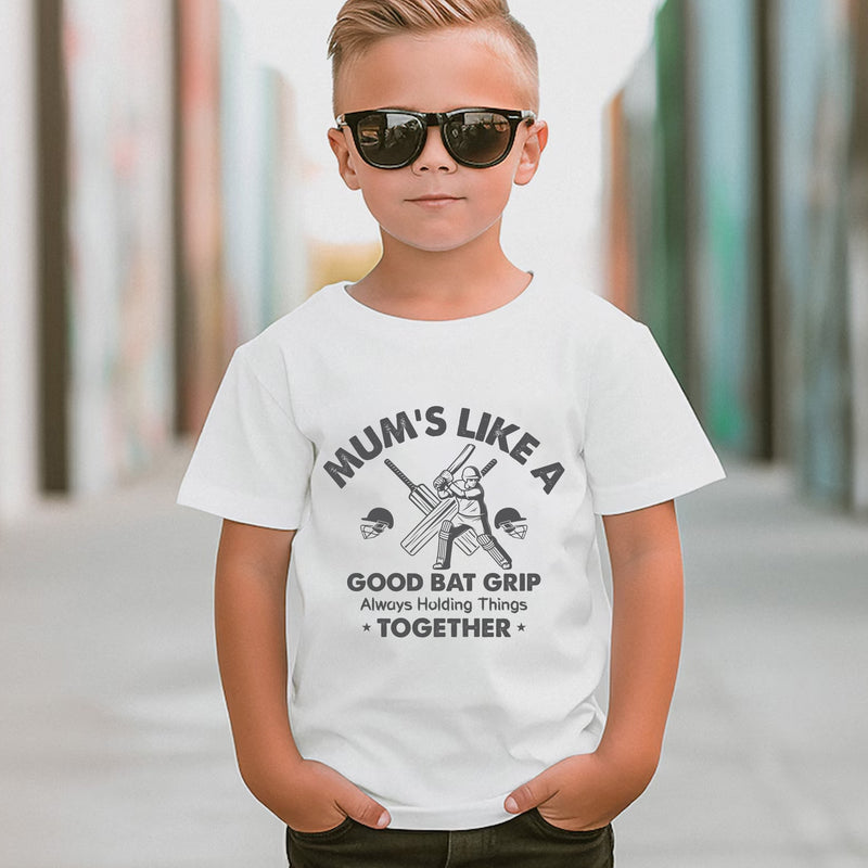 A little boy wearing a white t-shirt with Mums Like A Good Bat Grip, Always Holding Things Together on the front. A Funny Cricket T-Shirt, Premium Fabric, Multiple Junior Sizes, Perfect for Boys and Girls