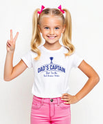 A little girl wearing a black t-shirt with Dad's Captain, But I'm The Real Decision-maker on the front. A Funny Cricket T-Shirt, Premium Fabric, Multiple Junior Sizes, Perfect for Boys and Girls