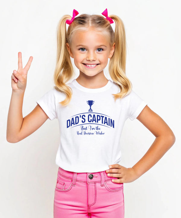 A little girl wearing a black t-shirt with Dad's Captain, But I'm The Real Decision-maker on the front. A Funny Cricket T-Shirt, Premium Fabric, Multiple Junior Sizes, Perfect for Boys and Girls