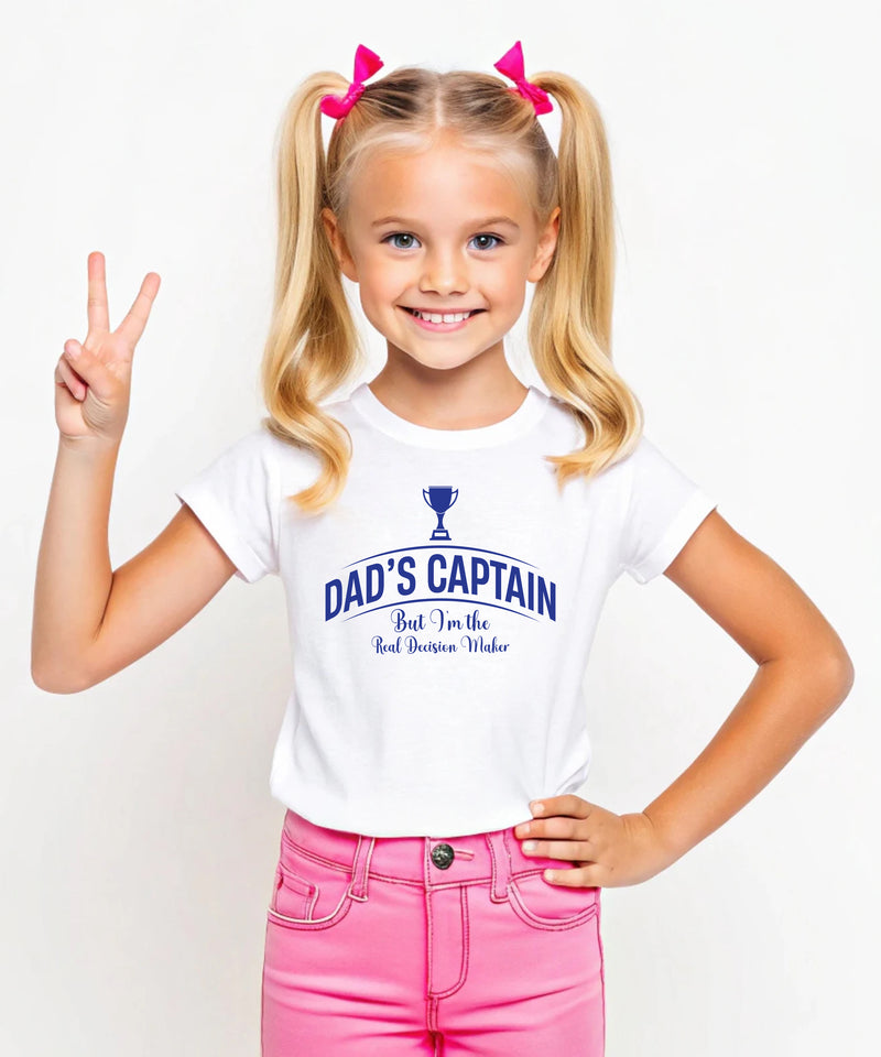 A little girl wearing a black t-shirt with Dad's Captain, But I'm The Real Decision-maker on the front. A Funny Cricket T-Shirt, Premium Fabric, Multiple Junior Sizes, Perfect for Boys and Girls