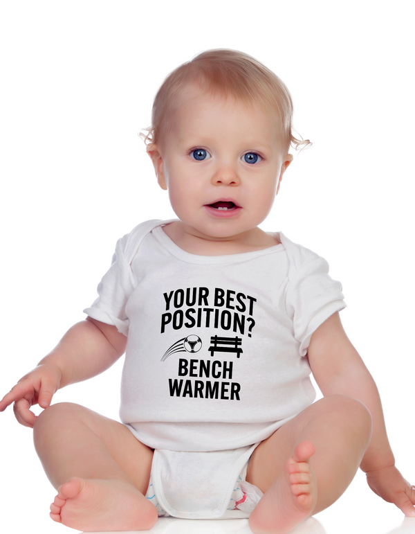 A little baby wearing a white baby grow with the funny football slogan on the front that reads 'Your Best Position? Bench Warmer'