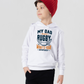 Child wearing a white hoodie with rugby-themed text on a plain, with a slogan on the front saying 'My Dad Plays Rugby. What’s Your Superpower?background