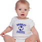 A little baby wearing a white baby grow with a funny football slogan on the front that reads 'Dribble You Can Barely Walk Straight!'