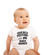 A little baby wearing a white baby grow with the funny football slogan on the front that reads 'Your Best Position? Bench Warmer'