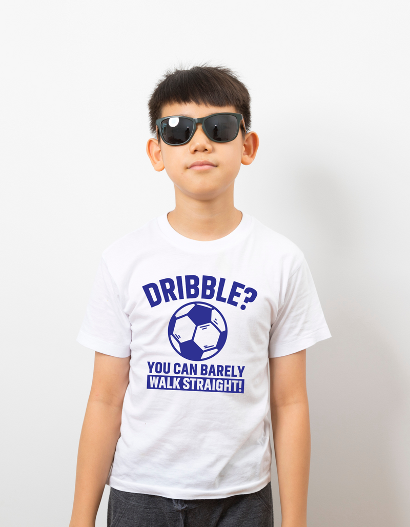 A little baby wearing a white t-shirt with a funny football slogan on the front that reads 'Dribble You Can Barely Walk Straight!'