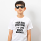 A little boy wearing a white t-shirt that has the funny football slogan on the front that reads 'Your Best Position? Bench Warmer'
