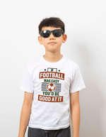A little boy wearing a white T-shirt with the funny football slogan on the front that reads 'If Football Was Easy You’d Be Good at It'