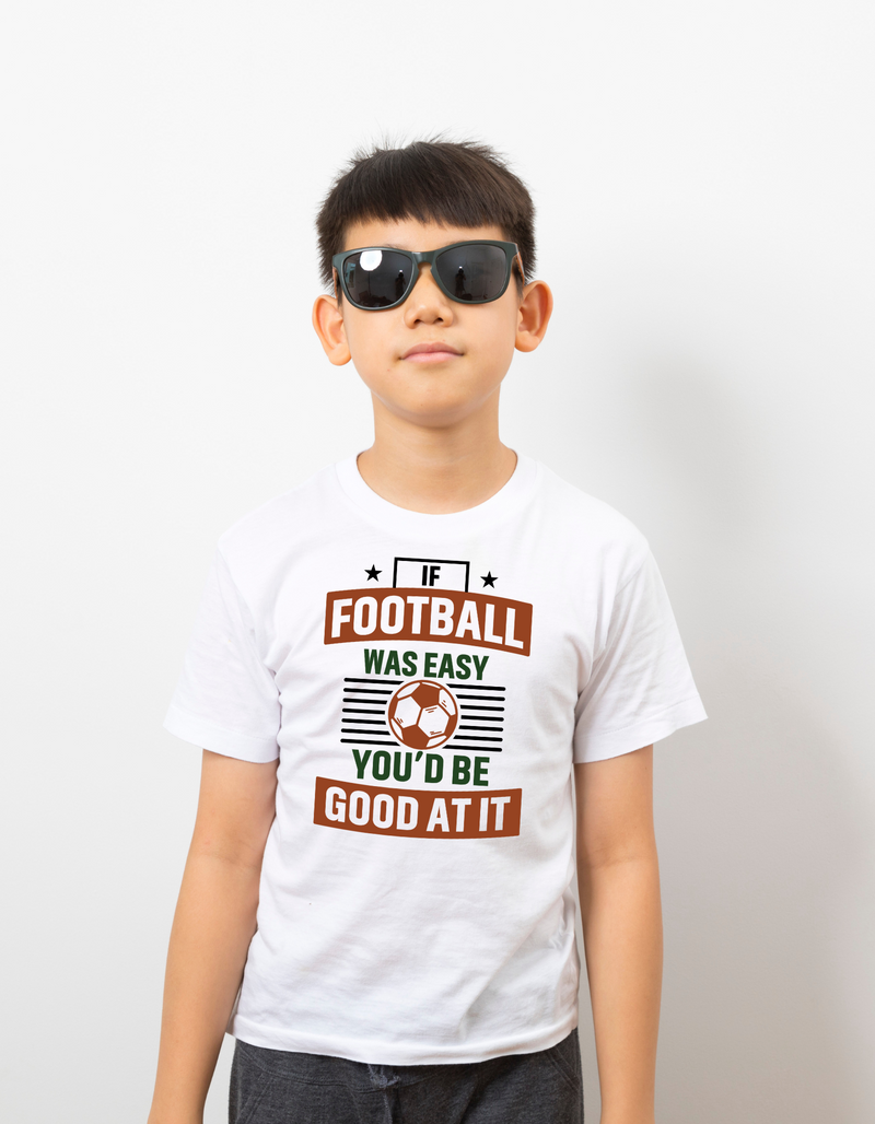 A little boy wearing a white T-shirt with the funny football slogan on the front that reads 'If Football Was Easy You’d Be Good at It'