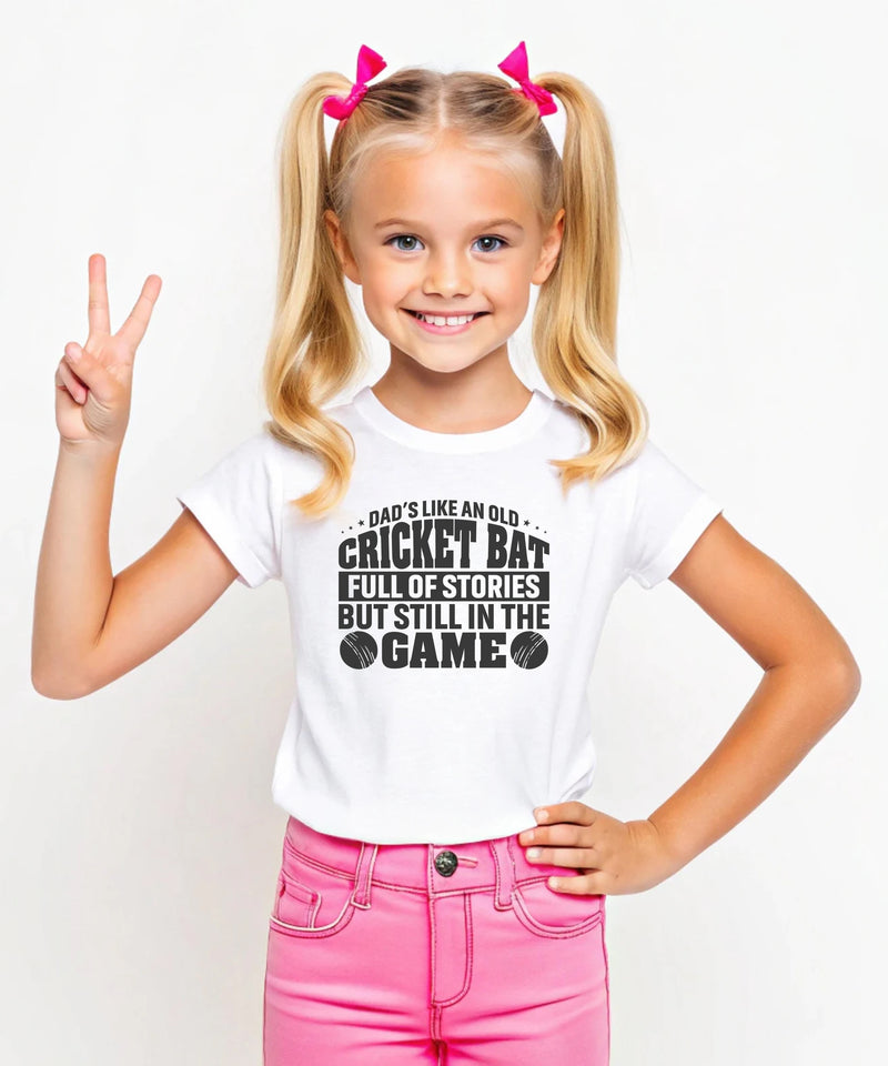 A little girl wearing a white t-shirt with Dads Like An Old Cricket Bat, Full Of Stories But Still In The Game on the front! A Funny Cricket Tee, Premium Fabric, Multiple Junior Sizes, Perfect for Boys and Girls
