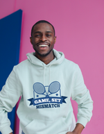 A man wearing a white hoodie that has a funny tennis slogan on the front that reads 'Game, Set, Mismatch'
