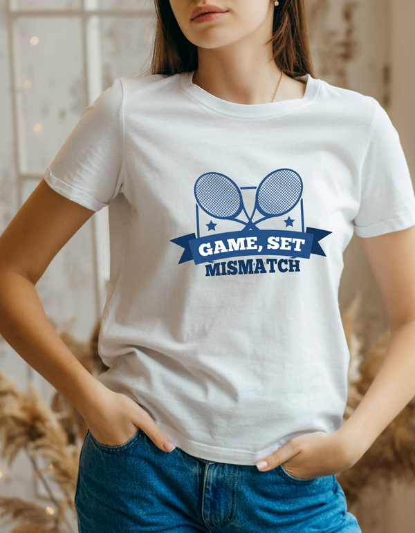 A lady wearing a white t-shirt that has a funny tennis slogan on the front that reads 'Game, Set, Mismatch'