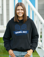 A lady wearing a black hoodie that has a funny tennis slogan on the front that reads 'Game, Set, Mismatch'