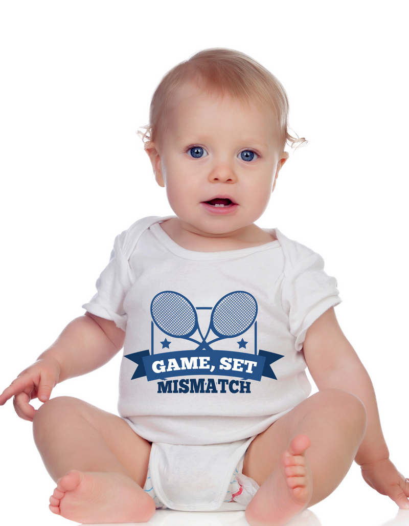 A little baby wearing a white baby grow with the funny tennis slogan on the front that reads 'Game, Set, Mismatch'