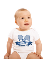 A little baby wearing a white baby grow with the funny tennis slogan on the front that reads 'Game, Set, Mismatch'