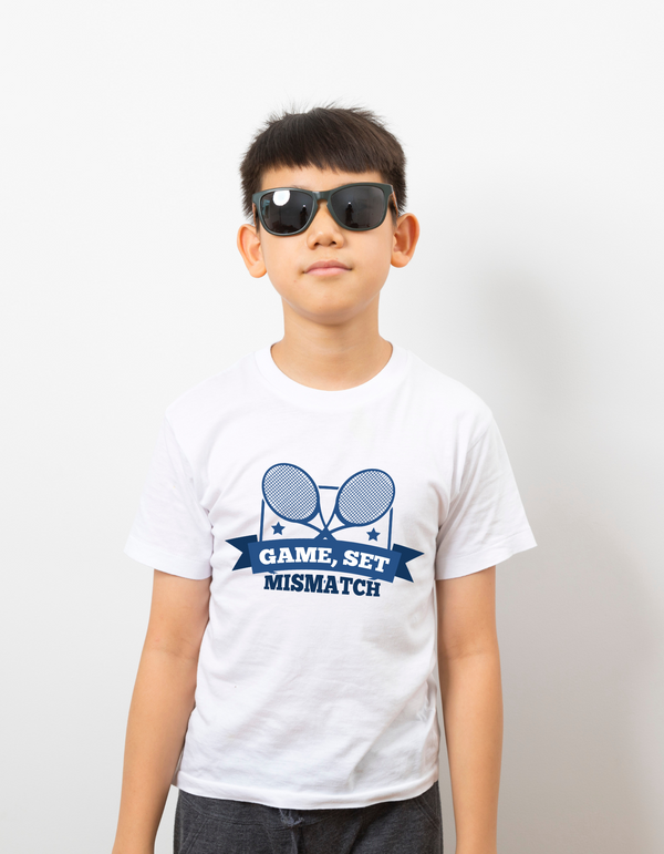 A boy wearing a white t-shirt with the funny tennis slogan on the front that reads 'Game, Set, Mismatch'