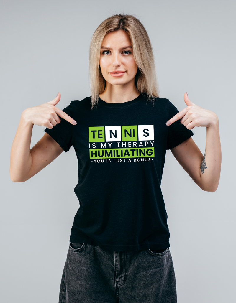 A lady wearing a black t-shirt with the funny tennis slogan on the front that reads 'Tennis Is My Therapy, Humiliating You Is Just A Bonus'