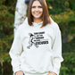 A lady wearing a white hoodie with a funny tennis slogan on the front that reads 'This Court Ain't Big Enough For Your Excuses'