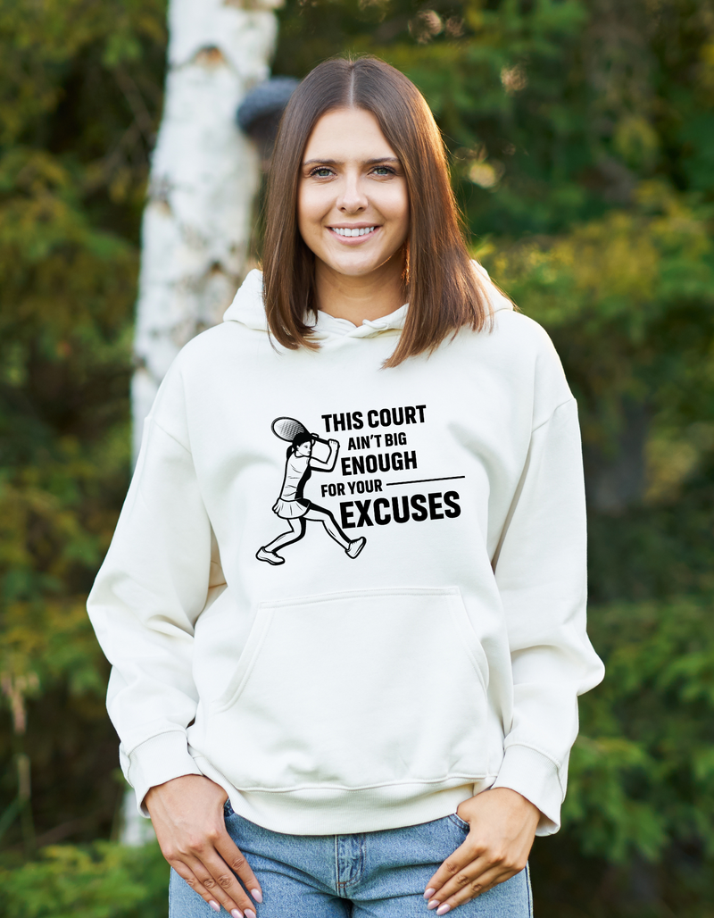 A lady wearing a white hoodie with a funny tennis slogan on the front that reads 'This Court Ain't Big Enough For Your Excuses'