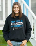 A lady wearing a black hoodie with the funny tennis slogan on the front which reads 'Your Serve Is Slower Than My Grandma's Wifi'
