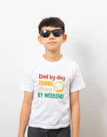 A boy wearing a white t-shirt with a funny tennis slogan on the front that reads 'Dad By Day, Tennis Champ By Weekend'