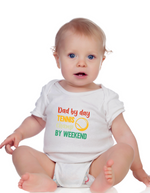 A little baby wearing a white baby grow with a funny tennis slogan on the front that reads 'Dad By Day, Tennis Champ By Weekend'
