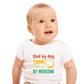 A little baby wearing a white baby grow with a funny tennis slogan on the front that reads 'Dad By Day, Tennis Champ By Weekend'