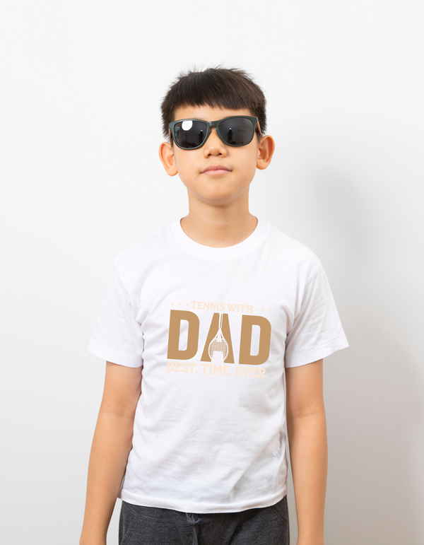A boy wearing a white t-shirt with the funny tennis slogan on the front that reads 'Tennis with Dad, BEST. TIME. EVER'