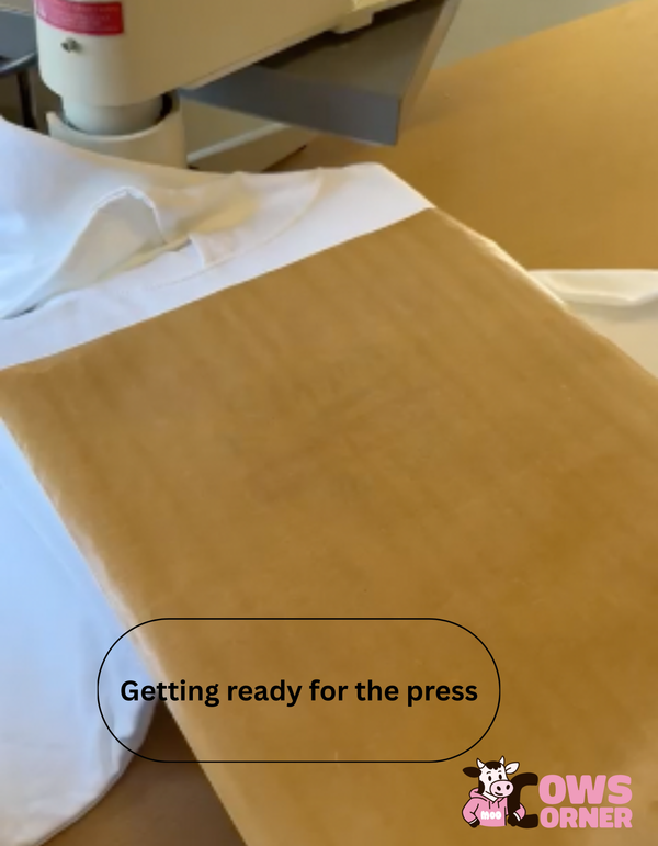Text 'Getting ready for the press' on a yellow surface with a white cloth over the Cows Corner garment
