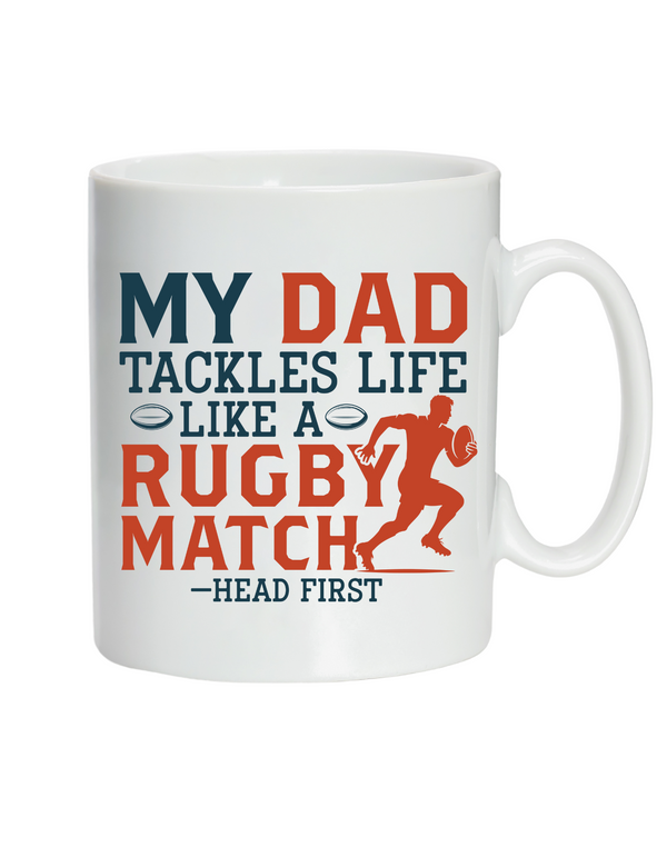 White mug with colorful text and rugby graphic on a white background with the Cows Corner slogan saying My dad tackles life like a rugby match - head first.