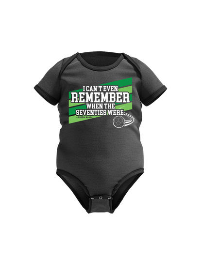 Black baby onesie with green and white text on a white background with Cows Corner slogan I can't even remember when the seventies were - Robbie Keane
