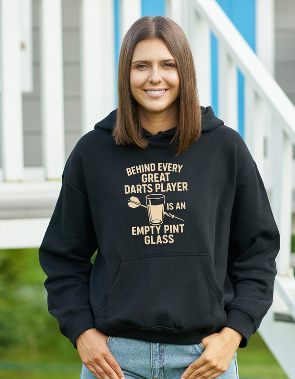 Person wearing a black hoodie with a humorous darts player quote, standing outdoors with a Cows Corner slogan saying Behind every great darts player is an empty pint glass