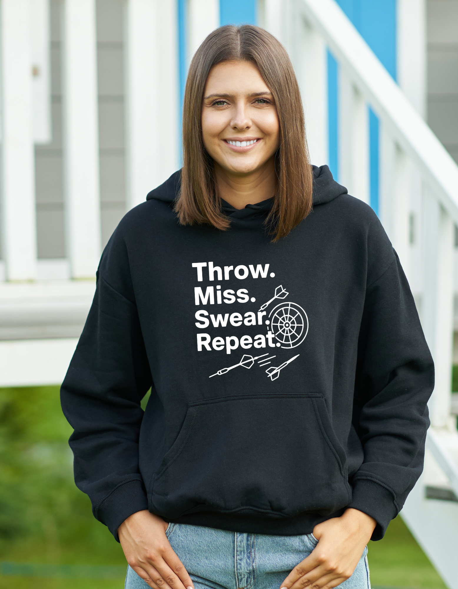 Woman wearing a black hoodie with text and graphics, standing outdoors with a Cows Corner slogan saying Throw, Miss, Swear, Repeat.