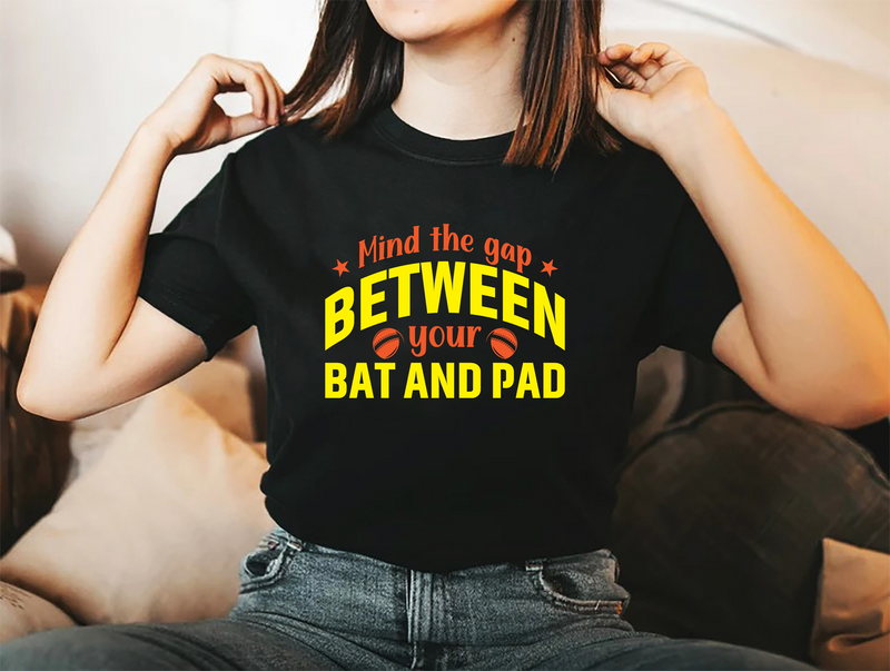 A lady wearing a black t-shirt with Mind The Gap Between Your Bat And Pads on the front. A Funny Cricket T-Shirt, Premium Fabric, Multiple Adult Sizes