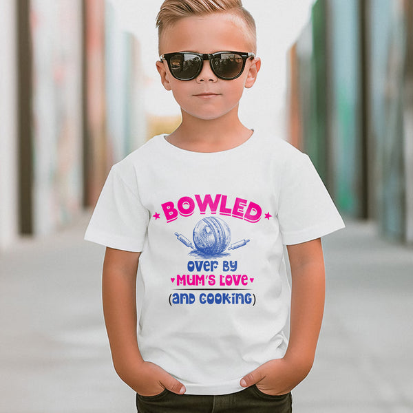 A little boy wearing a white t-shirt with Bowled Over by My Mum’s Love & Cooking on the front. A Funny Kids Cricket T-Shirt, Multiple Junior Sizes, Perfect for Boys and Girls