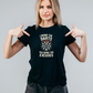 Woman wearing a black t-shirt with a dartboard graphic and text, pointing at the shirt with the cows corner slogan saying I Bring the Darts You Bring the Excuses