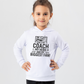 A little girl wearing a white hoodie with the funny football slogan on the front saying 'Messi, Ronaldo…Nah ’My Dads the Real Goat!