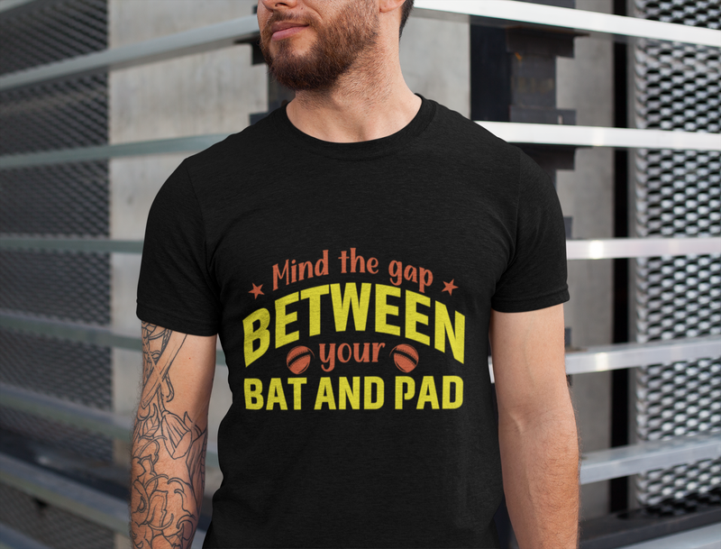 A man wearing a black t-shirt with Mind The Gap Between Your Bat And Pads on the front. A Funny Cricket T-Shirt, Premium Fabric, Multiple Adult Sizes