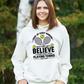 A lady wearing a white hoodie with funny tennis slogan on the front that reads 'A white ceramic mug with tennis slogan on the front that reads 'I Wake Up Every Morning and Still Can’t Believe I Actually Make a Living Playing Tennis.'