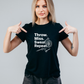 Woman wearing a black t-shirt with text and pointing at it, on a plain background with a Cows Corner slogan saying Let's play Darts I'll show you my best shaft work