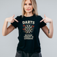 Woman wearing a black t-shirt with a dartboard graphic and text, pointing at the shirt with a Cows Corner slogan saying Darts because therapy is expensive.