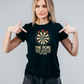 Woman wearing a black t-shirt with a dartboard graphic and text, pointing at the shirt with a Cows Corner slogan The oche where legends are made and excuses are born.