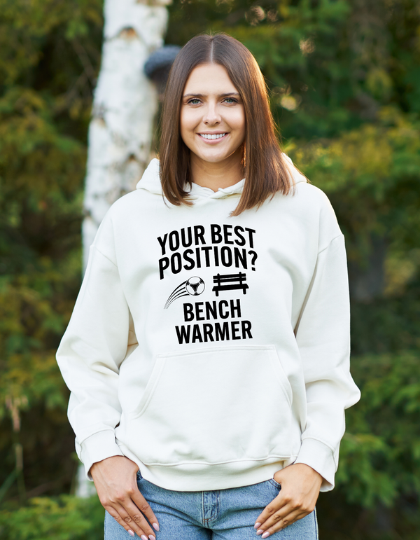 A lady wearing a white hoodie that has the funny football slogan on the front that reads 'Your Best Position? Bench Warmer'